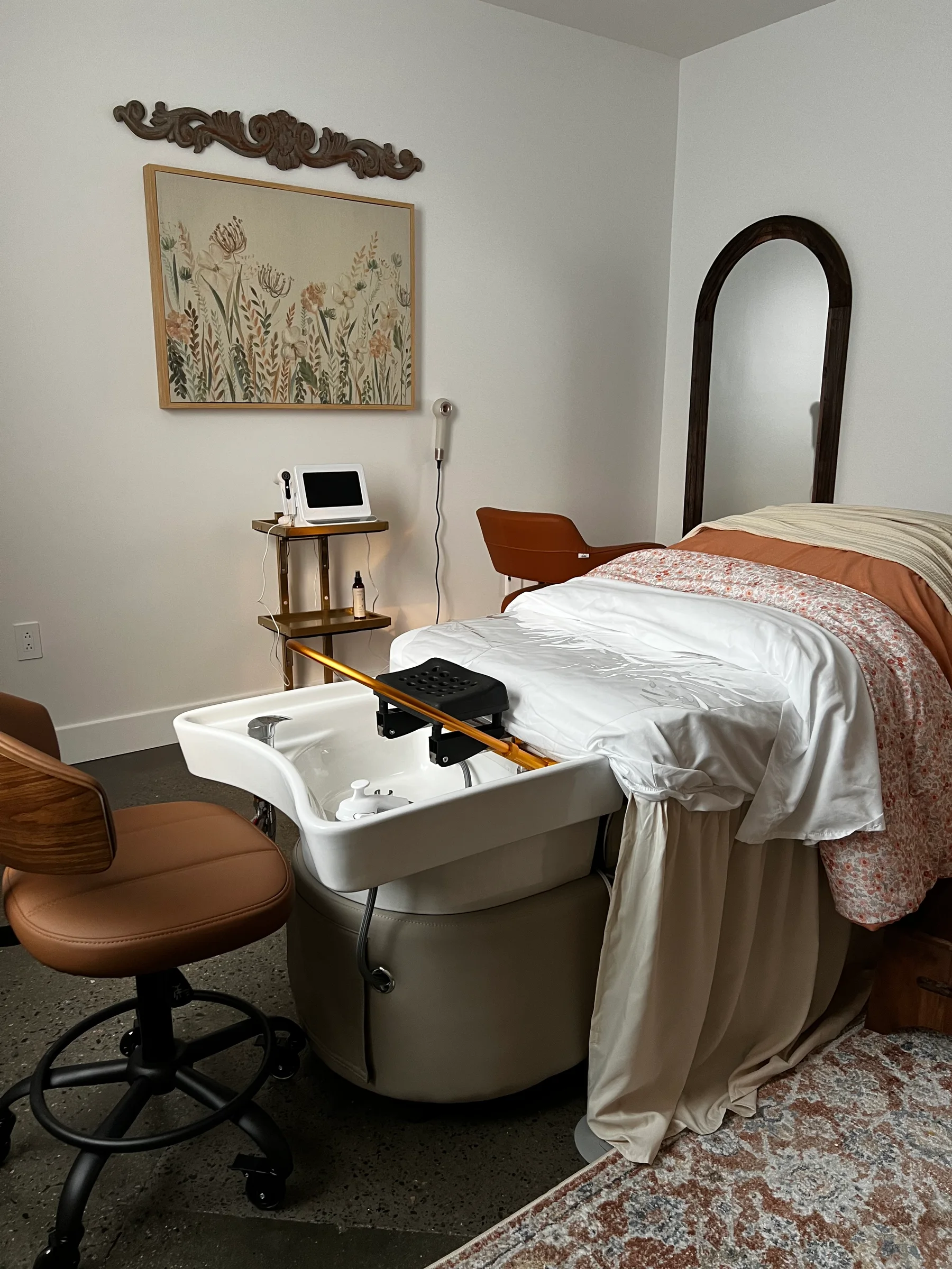 The head spa room at Southern Ground Esthetics with its white fresh-water basin, reclining spa bed layered in linens, and botanical artwork